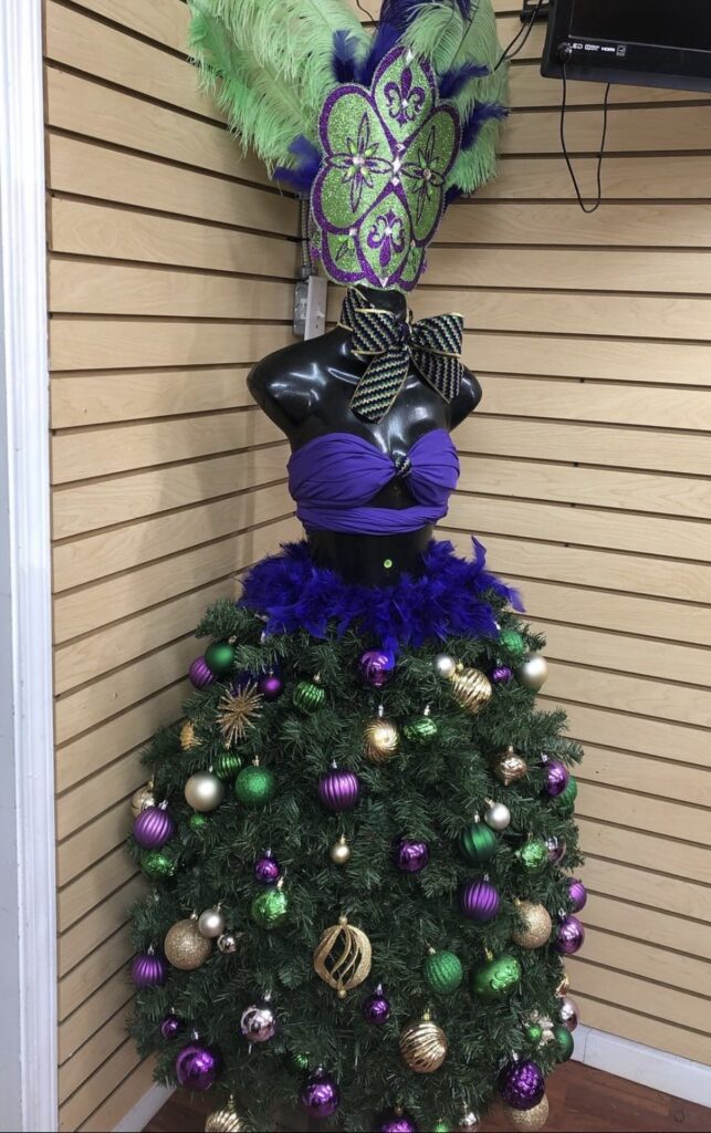Mardi Gras dress form “tree” with purple bodice, green and purple feathered headpiece, and ornaments around the skirt.