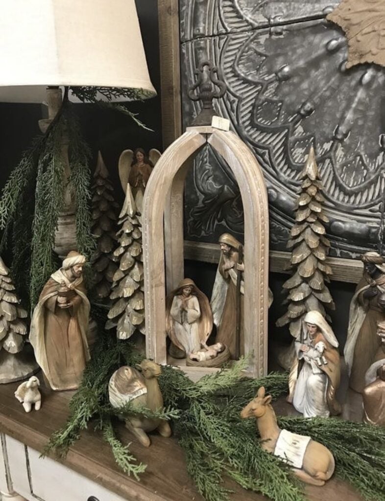 Detailed wood-tone nativity scene displayed with carved Christmas trees, greenery, an arched wooden stable, and an angel figure.