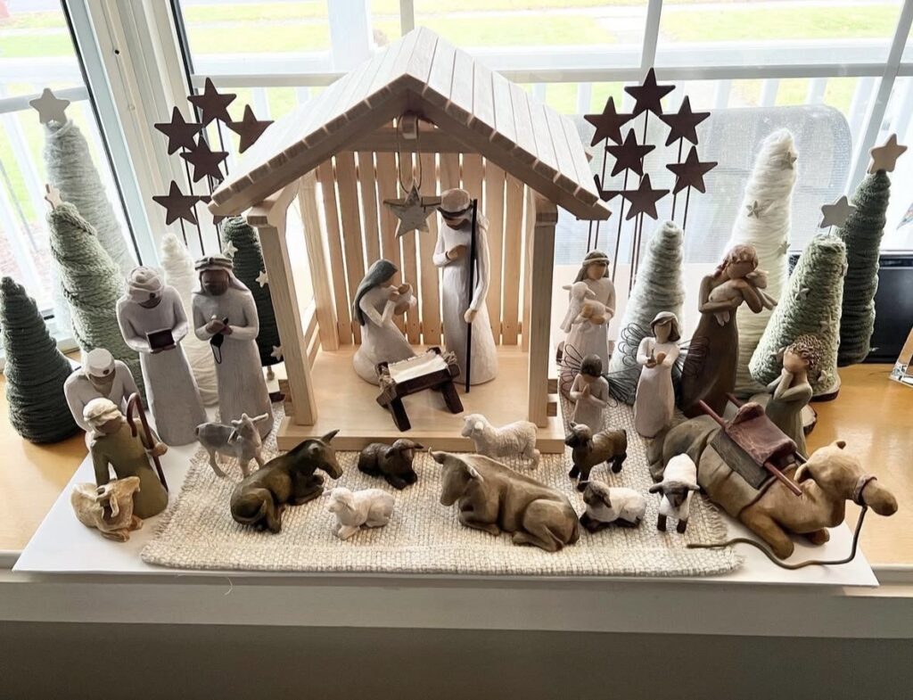 Large Willow-style nativity display arranged across a window ledge with a wooden stable, yarn-wrapped trees, shepherds, animals, and the Three Wise Men.