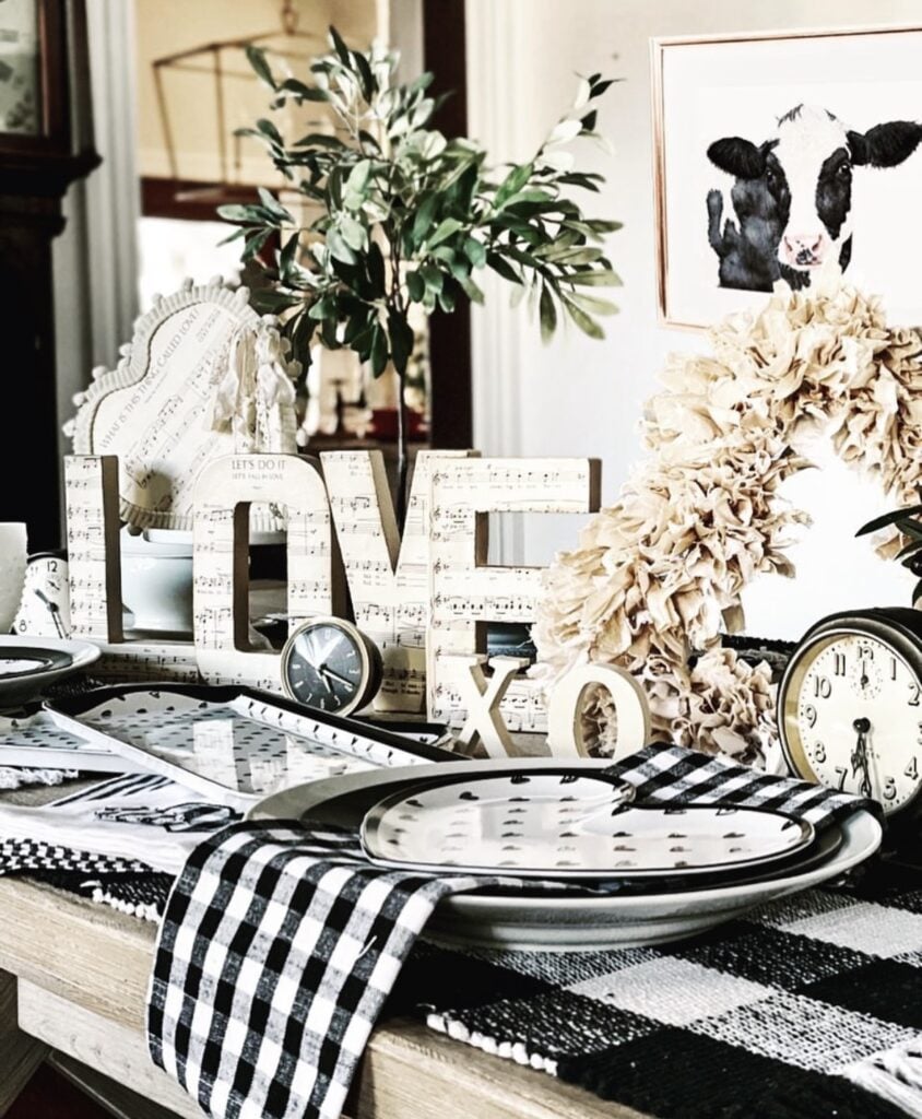 Modern neutral Valentine tablescape with black plates, heart napkins, candles, “XO” and “LOVE” accents, and a bold black-and-white runner.