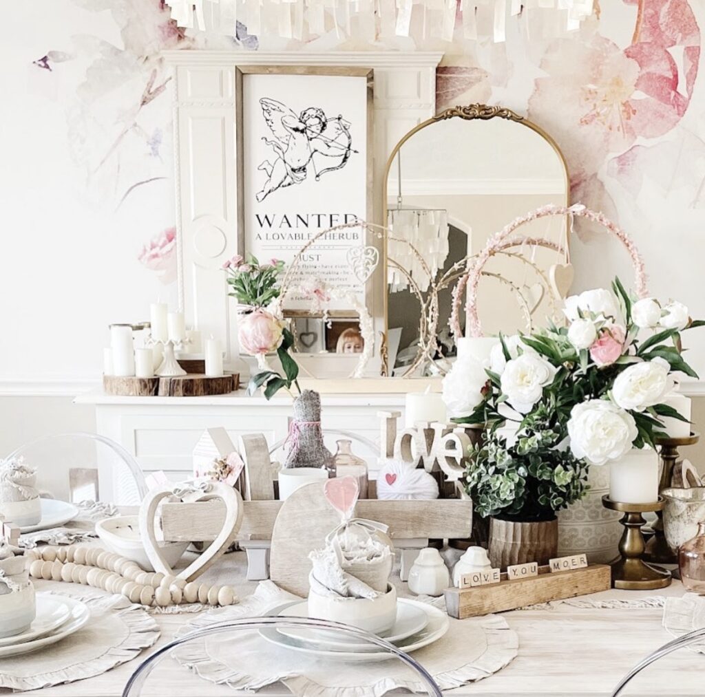 Romantic dining table setup with neutral decor, pink and white florals, a “love” sign, and soft Valentine accents.
