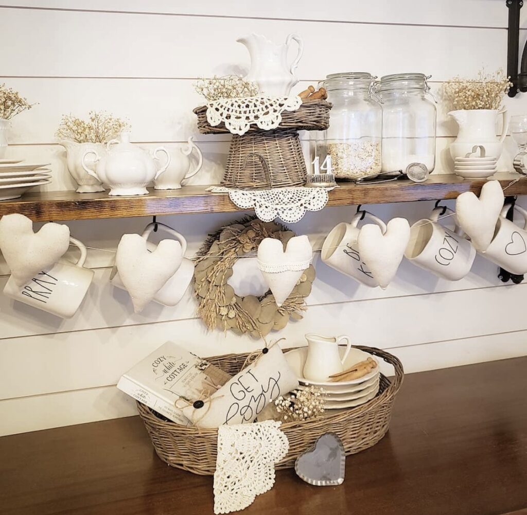 Farmhouse kitchen shelf styling with white pitchers, hanging heart mugs, wicker basket, and cozy neutral Valentine details.