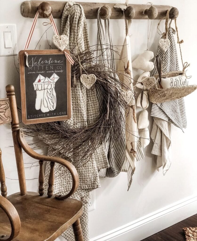 Entryway wall rack with a twig wreath, hanging heart ornaments, striped towels, and soft neutral farmhouse textures.