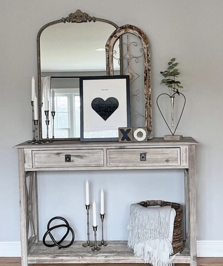 Neutral Valentine’s entryway console table with layered mirrors, framed black heart art, XO blocks, candlesticks, and a heart-shaped vase with greenery.