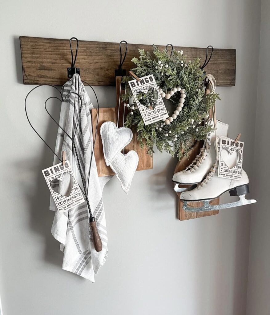 Farmhouse wall rack styled with a green wreath, bingo tags, white fabric hearts, cutting boards, and vintage white ice skates.