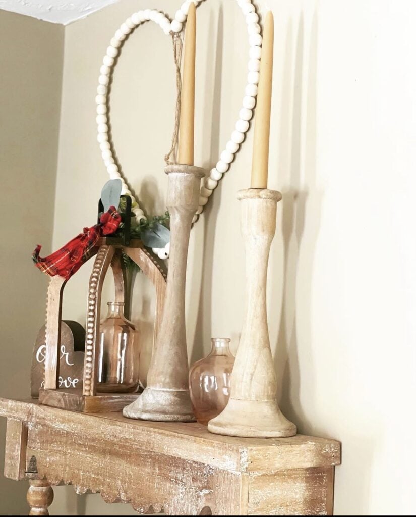 Rustic table with tall wooden candlesticks, a white bead heart garland, small glass vases, and subtle greenery for neutral Valentine style.