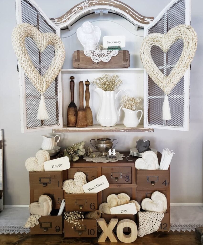 White farmhouse cabinet with woven heart hangings, vintage wooden drawers, fabric hearts, and XO letters.