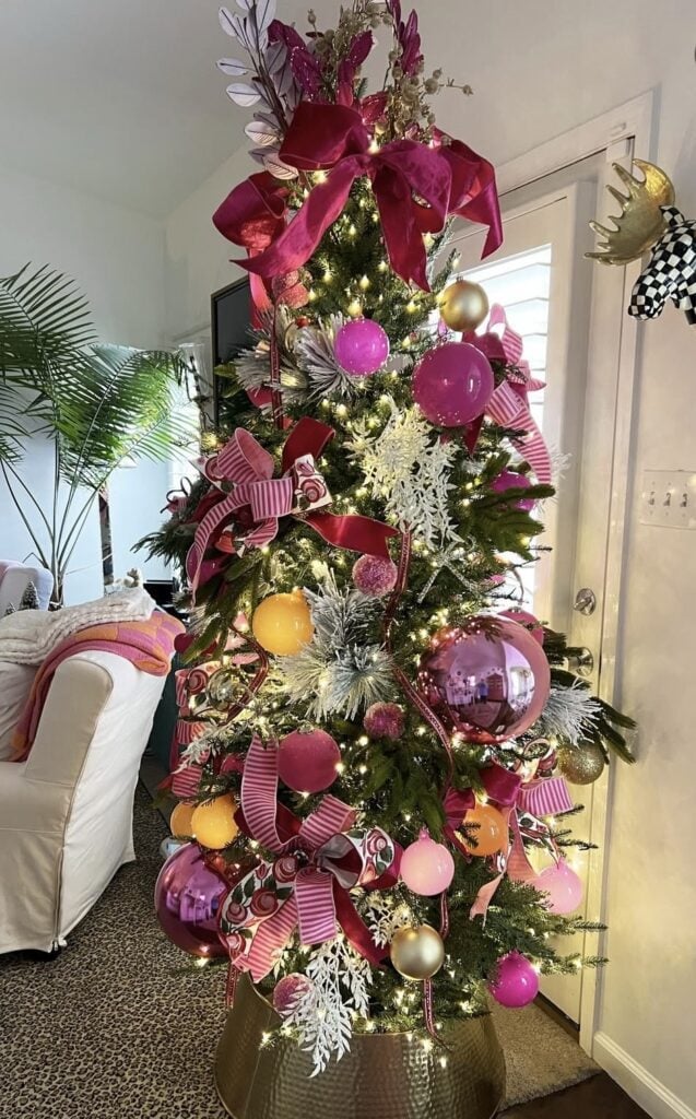 Green Christmas tree decorated with hot pink and burgundy ribbon, oversized pink ornaments, gold accents, and large white snowflakes.