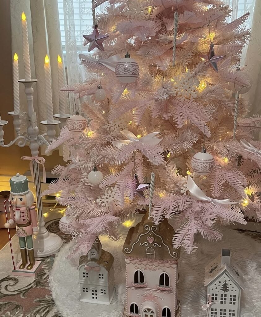 Pale pink artificial Christmas tree decorated with white bows, pink and white ornaments, snowflakes, and warm white lights