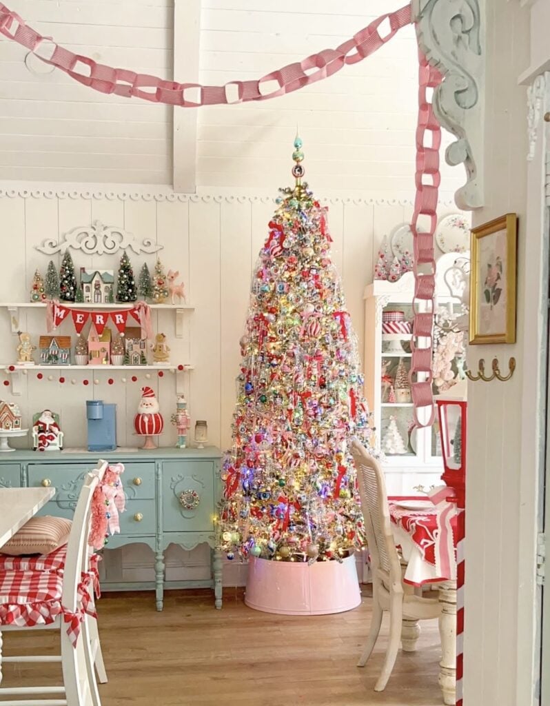 Colorful maximalist Christmas tree packed with vintage glass ornaments and tinsel in a cheerful red, pink, and pastel holiday room.