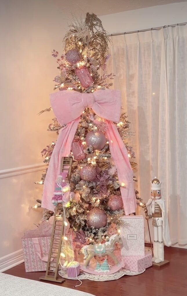 Pink Christmas tree decorated with playful ornaments beneath an oversized pink bow beside a retro pink holiday display.