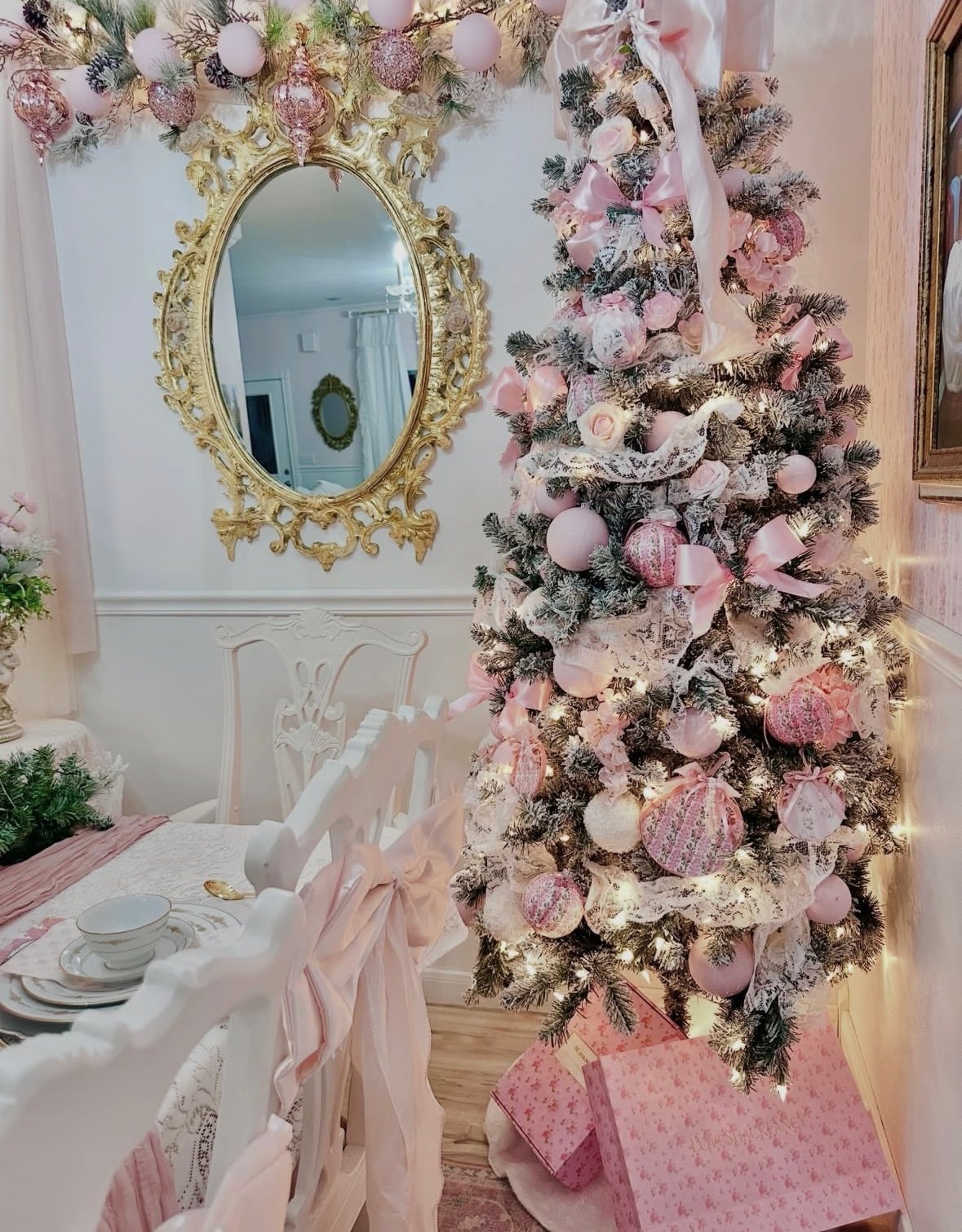 Flocked Christmas tree decorated with blush pink bows, lace ribbon, roses, and pink ornaments beside an ornate gold mirror.