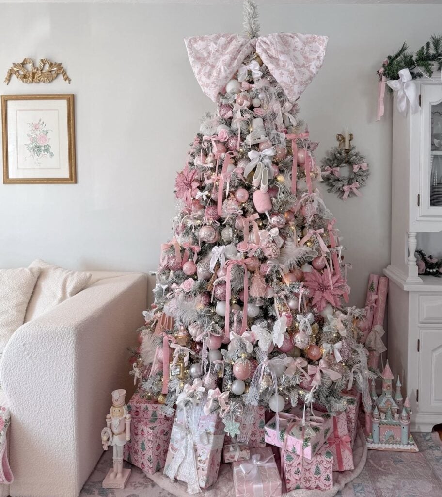 Flocked Christmas tree covered in blush pink and white ornaments, ribbons, whimsical decorations, and an oversized floral pink bow.