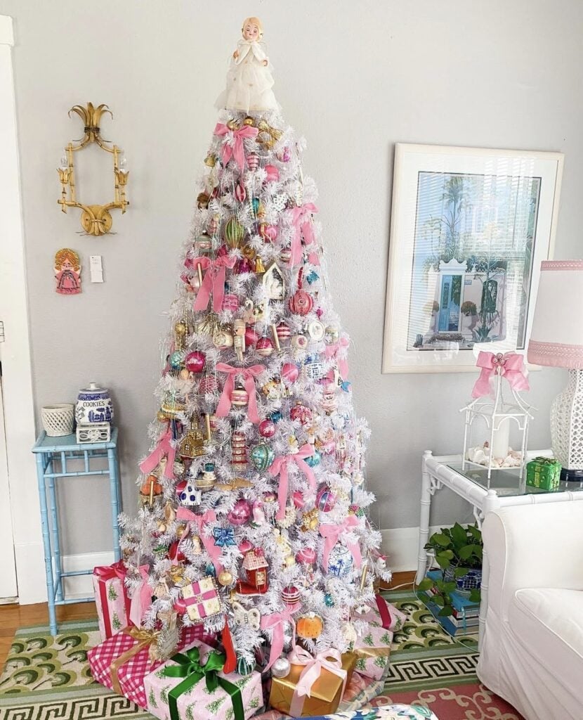 White Christmas tree packed with colorful vintage ornaments, pink ribbon bows, and whimsical decorations with wrapped gifts underneath.