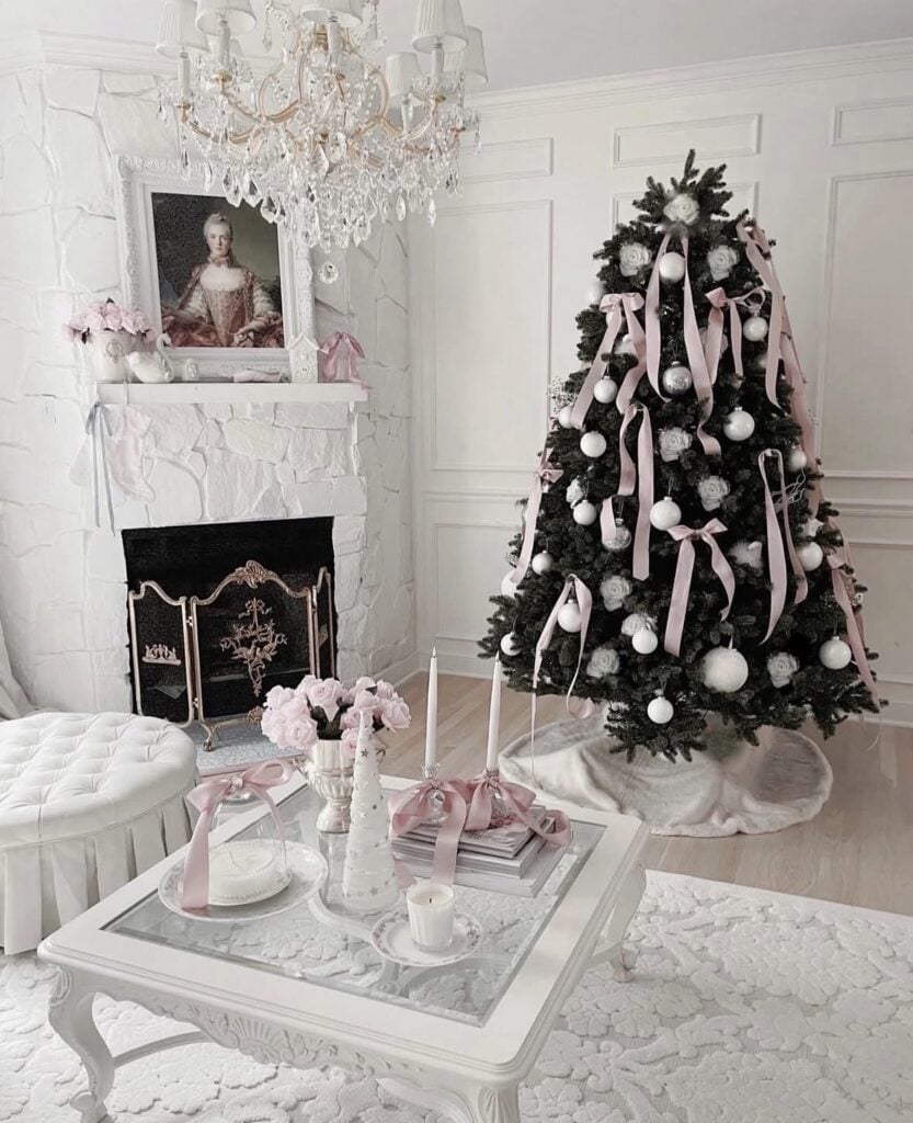 Elegant dark green Christmas tree decorated with pale pink ribbon bows, white ornaments, and soft pink flowers in a glamorous white living room.