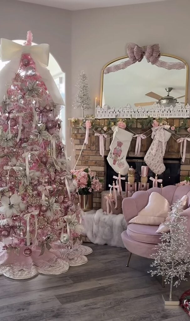Glamorous pink Christmas tree covered in blush ornaments, ribbons, florals, and a dramatic oversized white bow topper.
