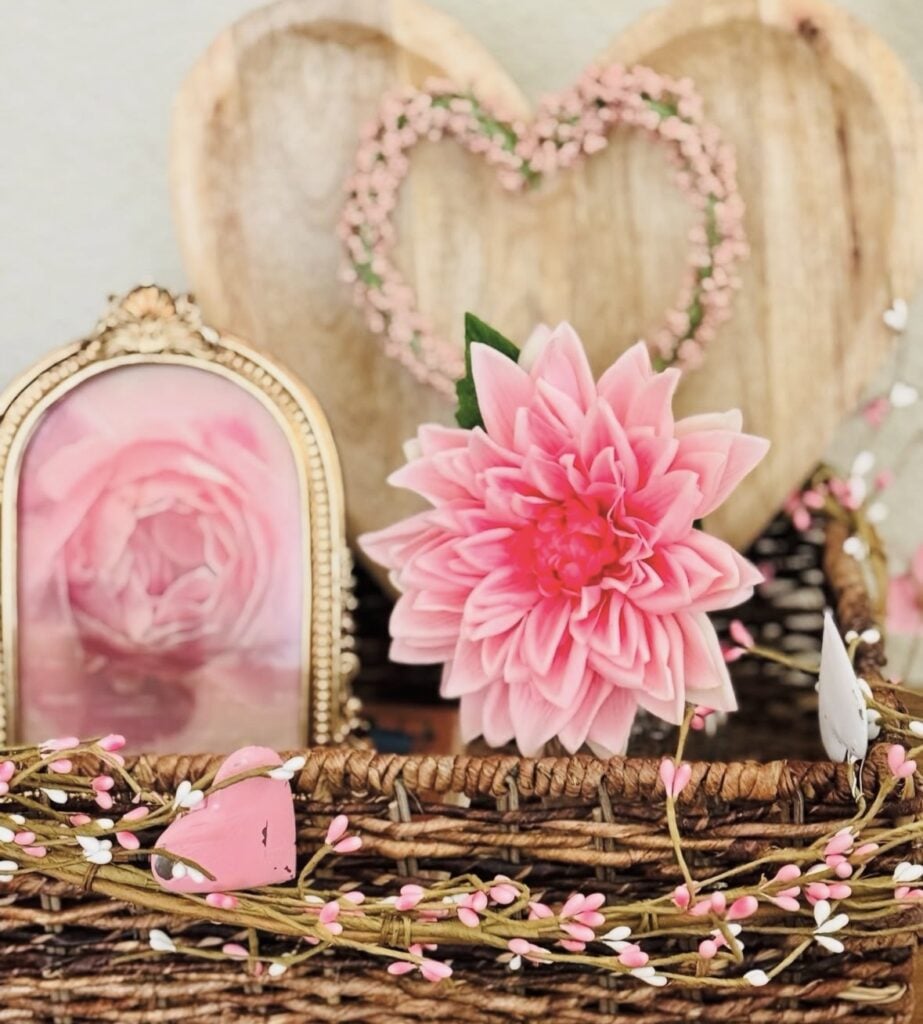 Wicker tray Valentine decor with a framed pink rose print, oversized blush pink flower, and rustic heart backdrop with a delicate pink berry heart garland.