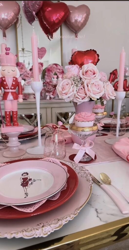 Glam pink and red Valentine table decor with heart balloons, tall pink taper candles, rose centerpiece, and layered plates with romantic details.