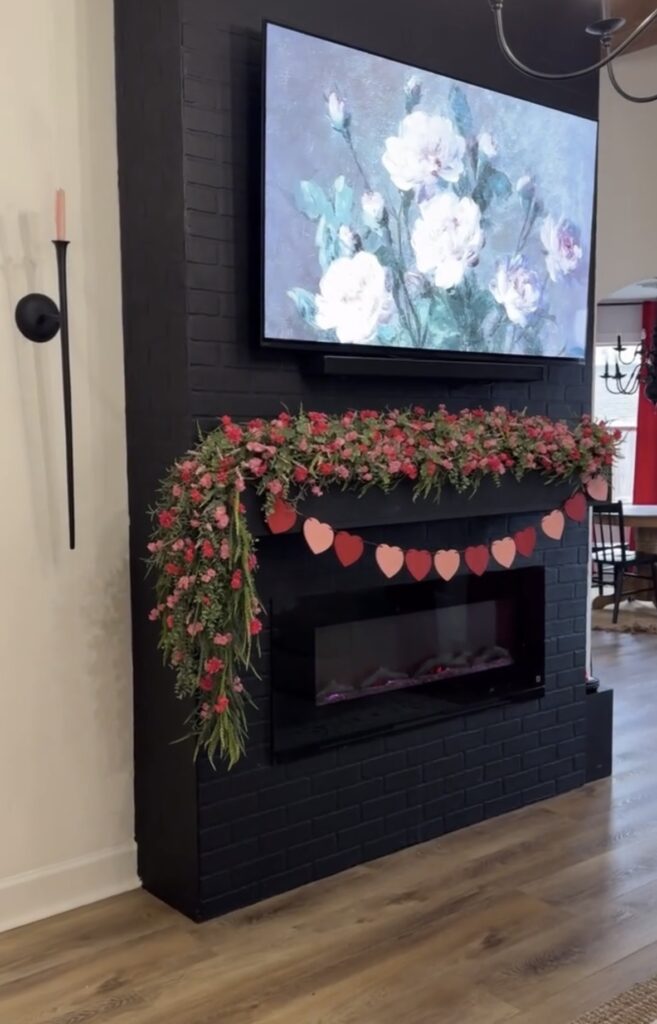 Modern black fireplace with floral Valentine garland and heart bunting under a mounted TV.