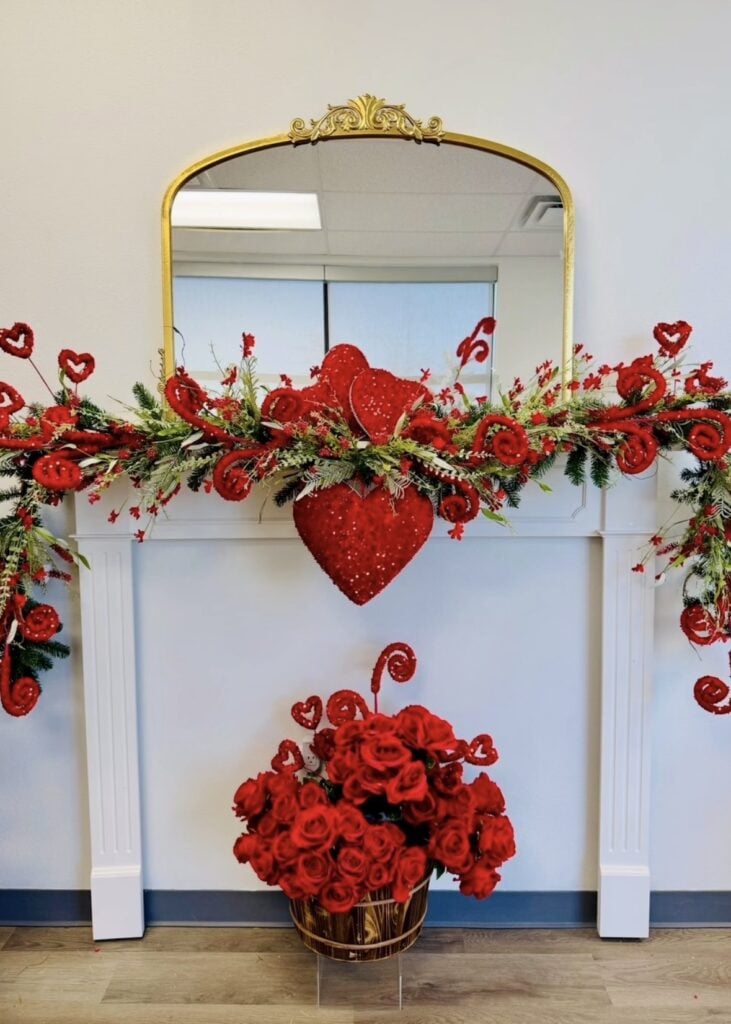White mantel with gold mirror, red heart garland, and a basket of red roses below.