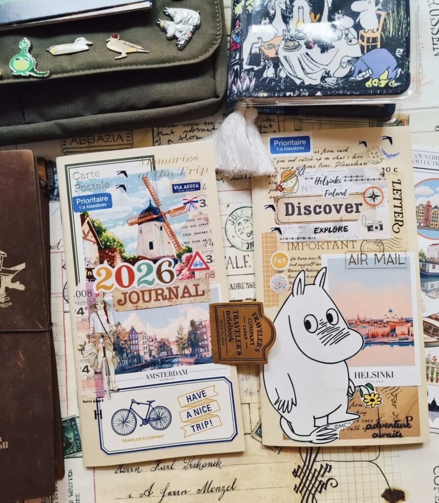 Travel journal cover collage labeled “2026 Journal” and “Amsterdam,” with postcard art, postage stamps, and a “Have a nice trip” ticket, plus a Moomin character and Helsinki air mail photo card.
