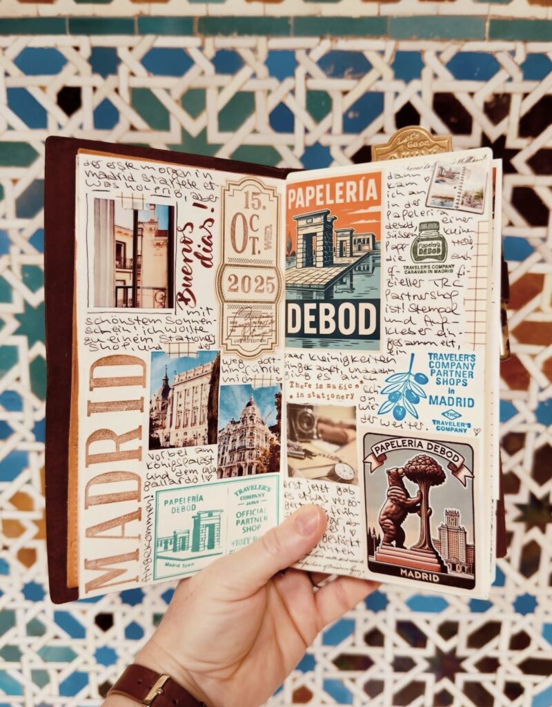 Hand holding a travel journal in front of a tile mosaic with the word MADRID and images with writing in the journal