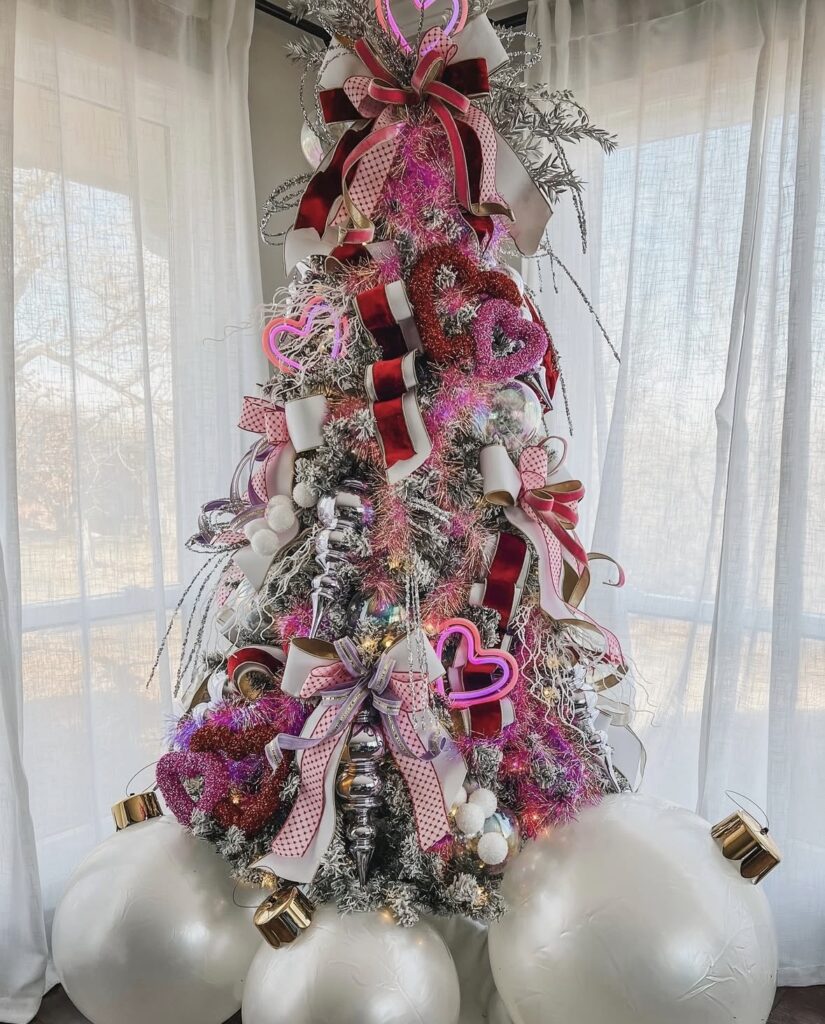 Tall Valentines Day tree decorated with pink ornaments, heart garlands, and ribbon in a cozy room, credit tinsel_and_trees.