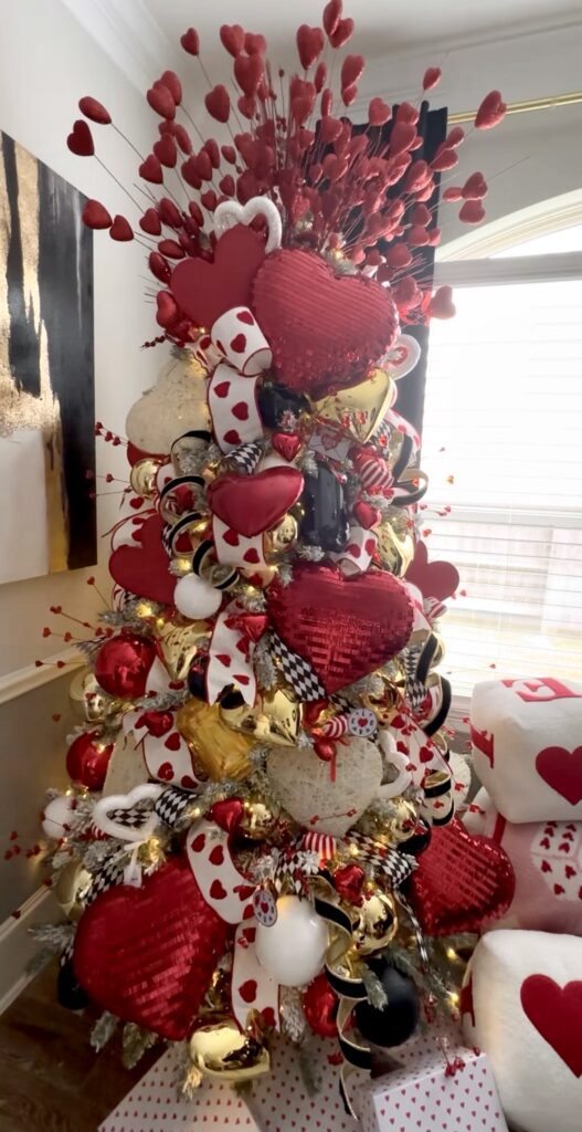 Queen of Hearts styled Valentines Day tree with clustered heart ornaments, ribbon, and matching decor at the base, credit styledholidaydecor.