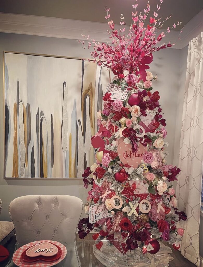 Cozy Valentines Day tree with layered ribbon, hearts, and roses with heart toppers beside a neutral sofa, credit christyandco74.