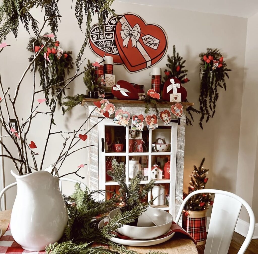 Vintage Valentine dining corner with a distressed cabinet, red heart decorations, mini trees, classic Valentine cards, and red plaid accents.