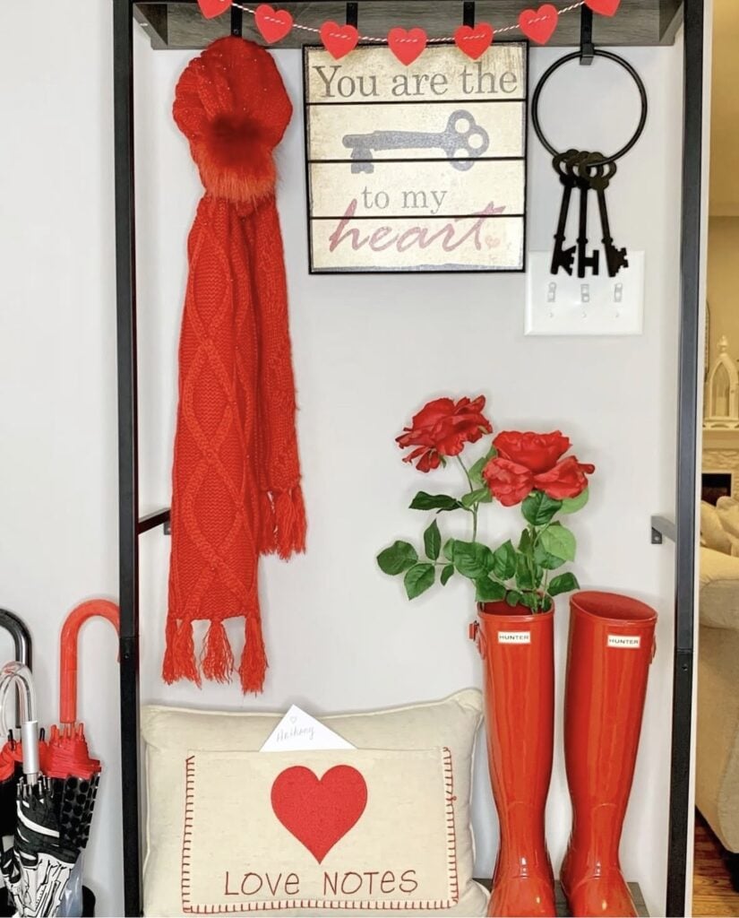 Valentine entryway setup with a red scarf, heart garland, “You are the key to my heart” sign, red rain boots, and a “LOVE NOTES” pillow.