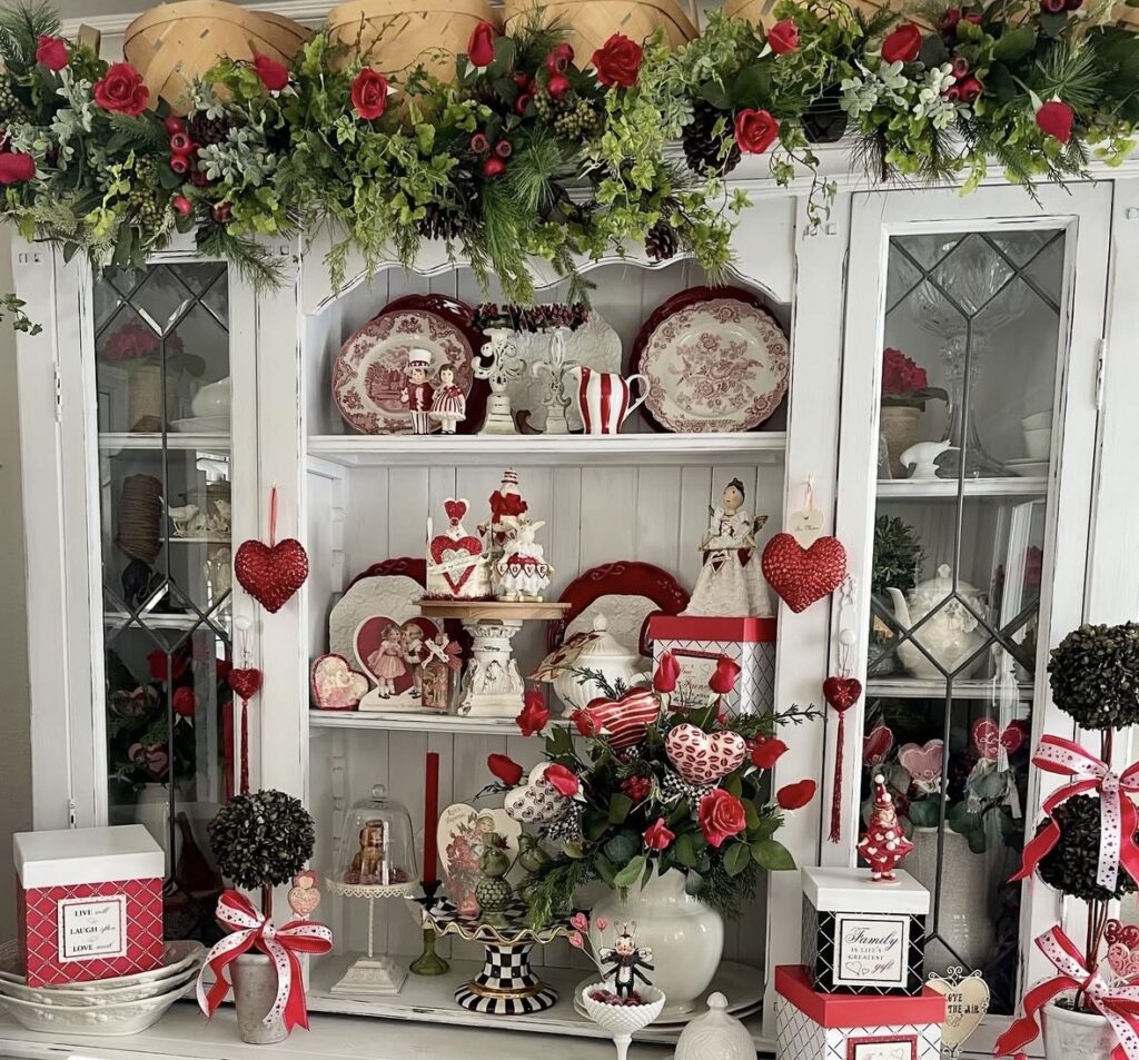 White hutch styled for Valentine’s Day with red heart ornaments, floral picks, and vintage-inspired decor.