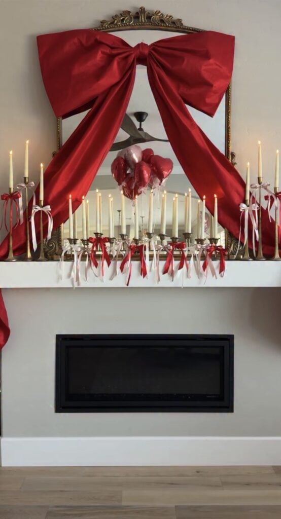 Red Valentine mantle with oversized bow on mirror and rows of ribbon-tied taper candles.