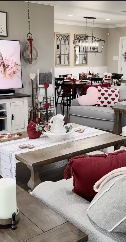 Cozy living room decorated for Valentine’s Day with heart pillows, red accents, and a set dining table.