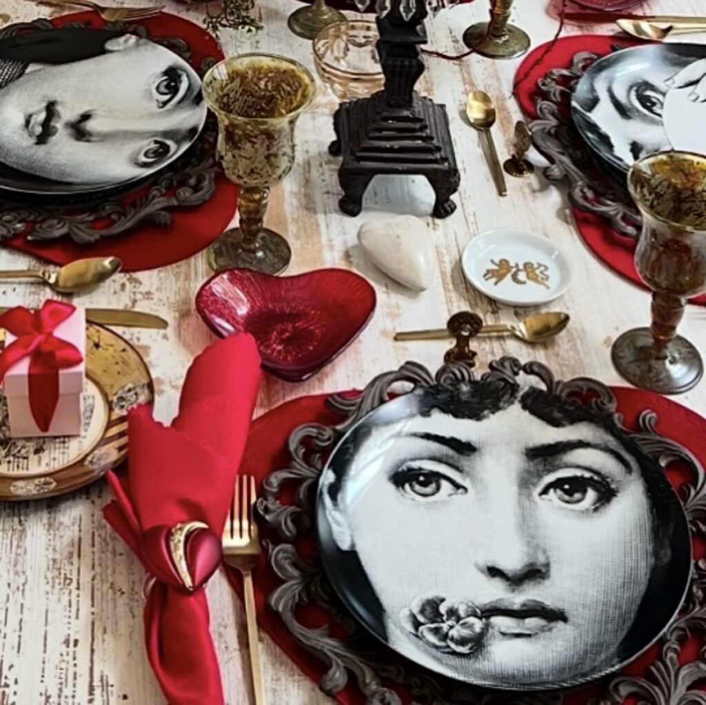 Romantic red Valentine tablescape with bold red chargers, gold flatware, heart decor, and vintage-style face plates.