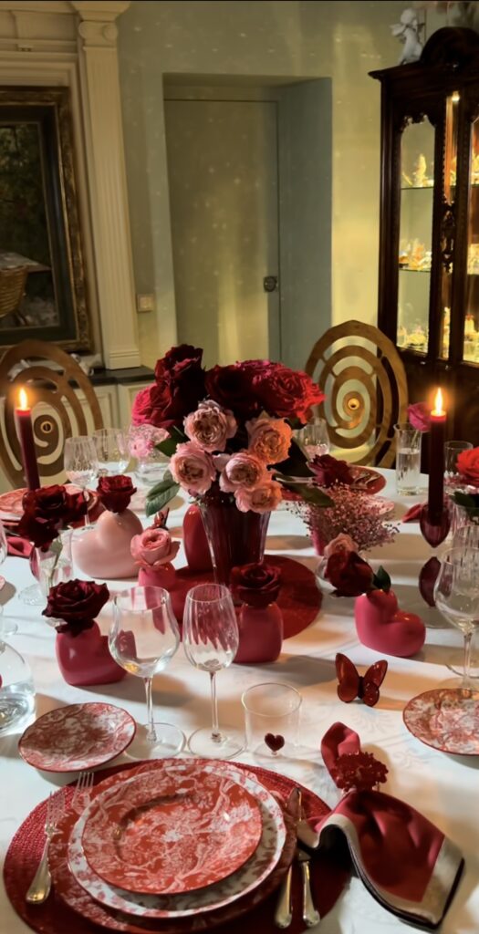 Elegant Valentine dinner table with red and pink rose centerpieces, tall candles, and romantic red place settings.