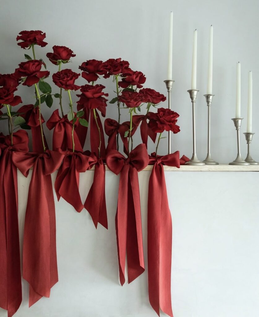 Minimalist red Valentine mantel shelf with deep red roses, oversized satin bows, and tall white taper candles.