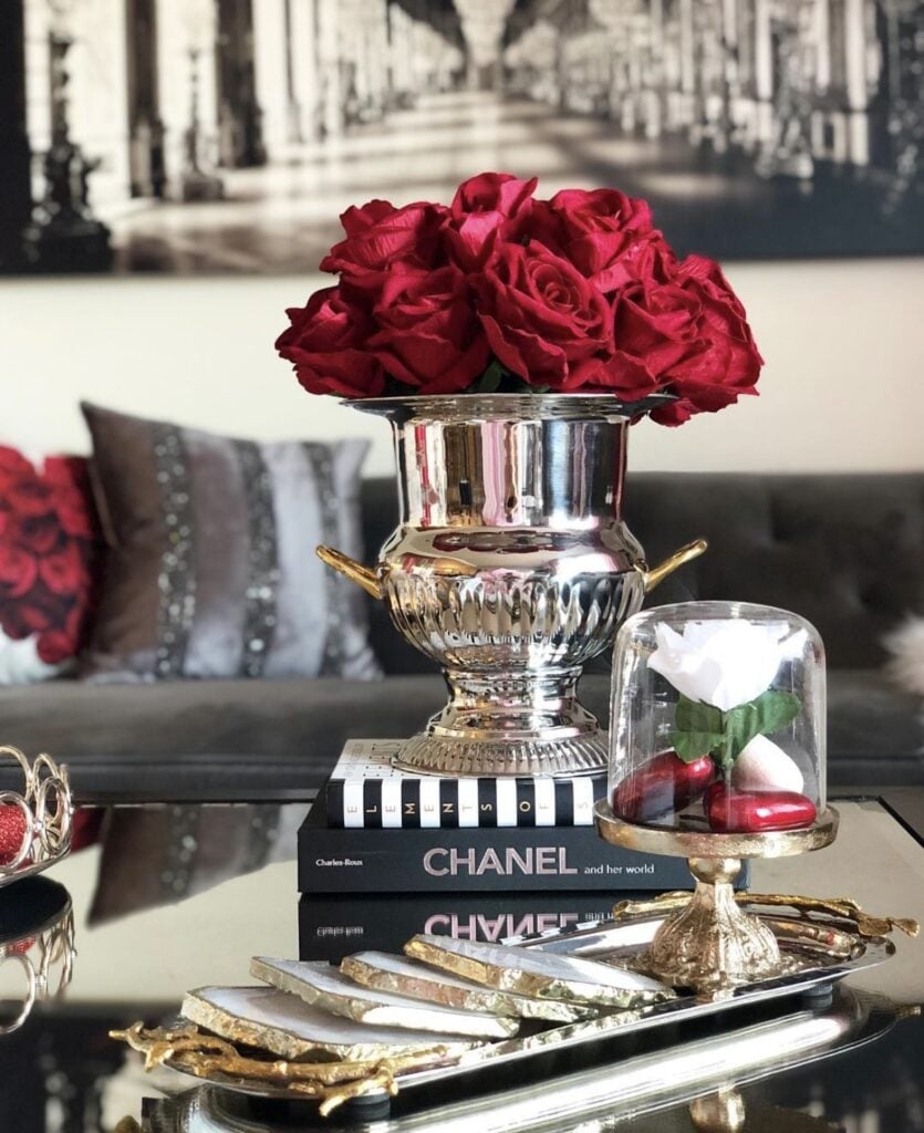Glam Valentine coffee table decor with a silver vase of red roses on stacked books and a cloche with a white rose.
