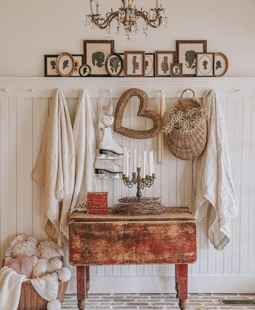 Cozy neutral Valentine’s wall and table setup with a woven heart, vintage ice skates, white taper candles, and soft neutral textiles.