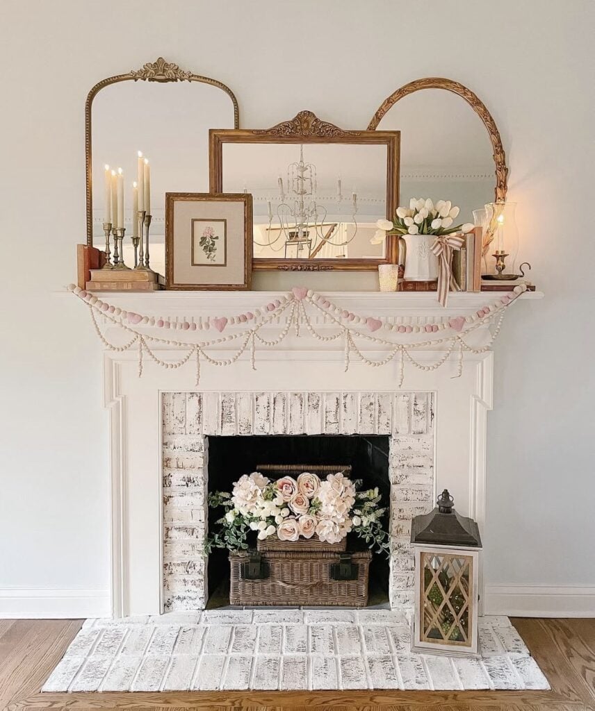 Neutral Valentine’s fireplace mantel with mirrors, candles, tulips, and a pink and white garland draped across the mantel.