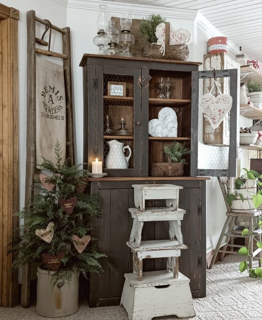 Farmhouse hutch styled for neutral Valentine’s Day with heart decor, candles, white pitchers, greenery, and a rustic step stool.
