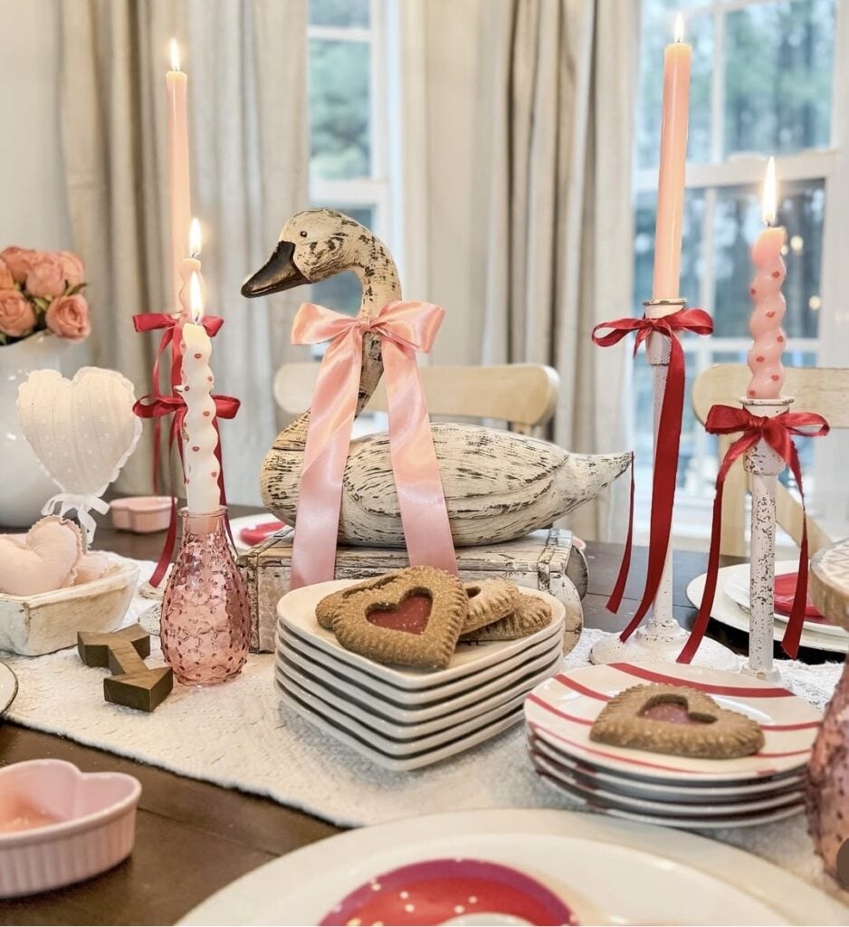 Red and pink Valentine table decor with a romantic tablescape featuring a swan, layered place settings, and heart-themed accents.