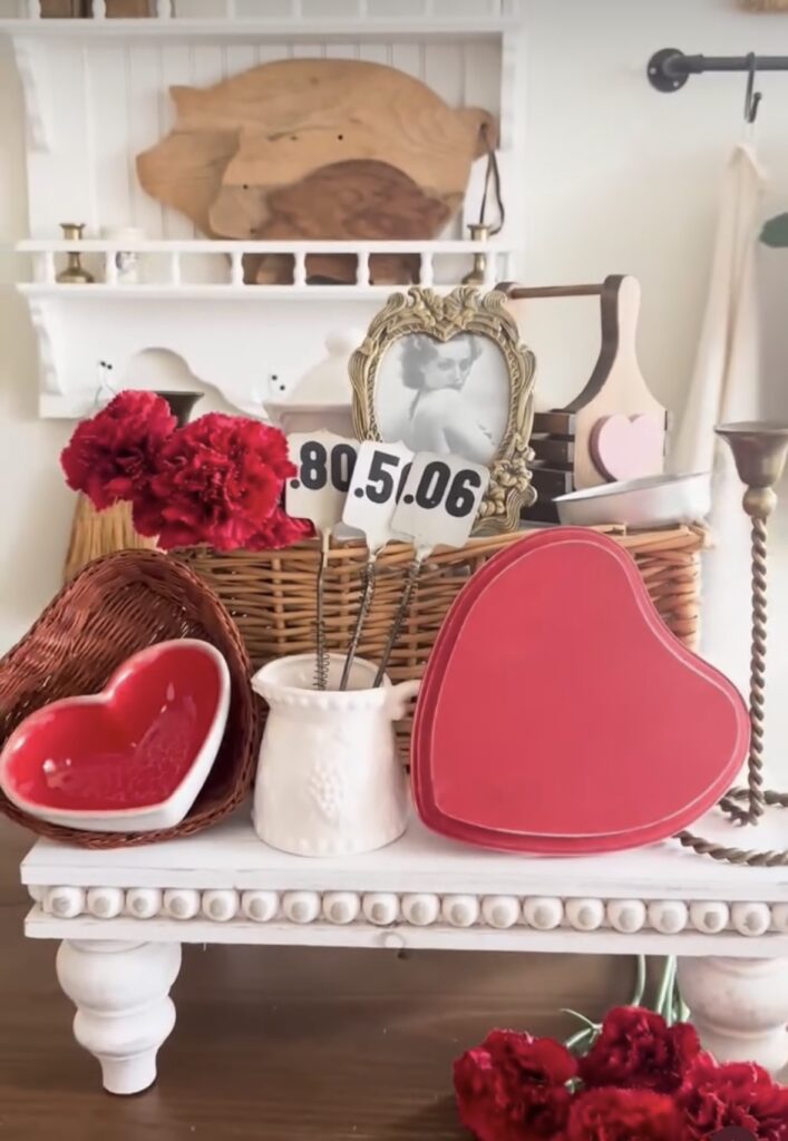Valentines day decor on a white tray with heart bowl, wooden heart, white vase with flowers and vintage picture in gold frame