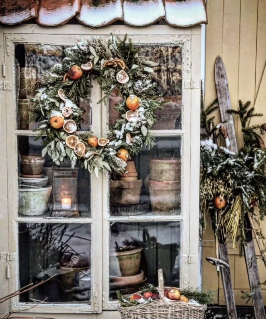Rustic fireplace mantel decorated with evergreen garland, candles, lanterns, and natural Winter Solstice decorations.