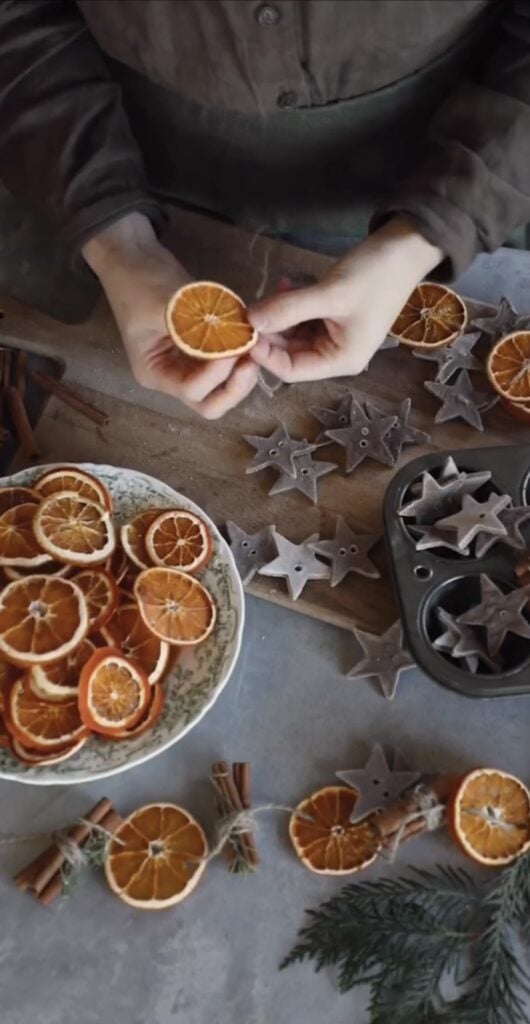 Rustic Winter Solstice table with oranges and stars with person making them into decorations celebrating the return of the light.