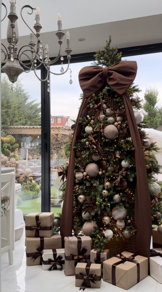 Brown Christmas tree decorated with layered neutral ornaments, oversized dark brown bow topper and warm holiday accents