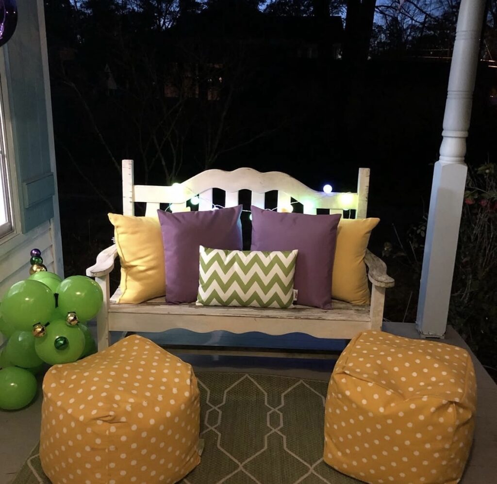 Cozy Mardi Gras white porch swing decorated with purple and gold pillows with a green balloon dog side table