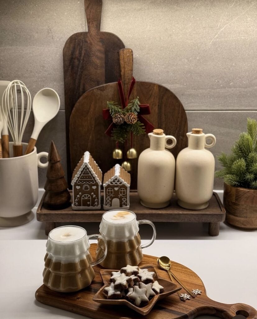 Gingerbread Christmas coffee station with layered cutting boards, gingerbread houses, lattes, and star-shaped cookies on a wood counter, featured by slowestuff.com.