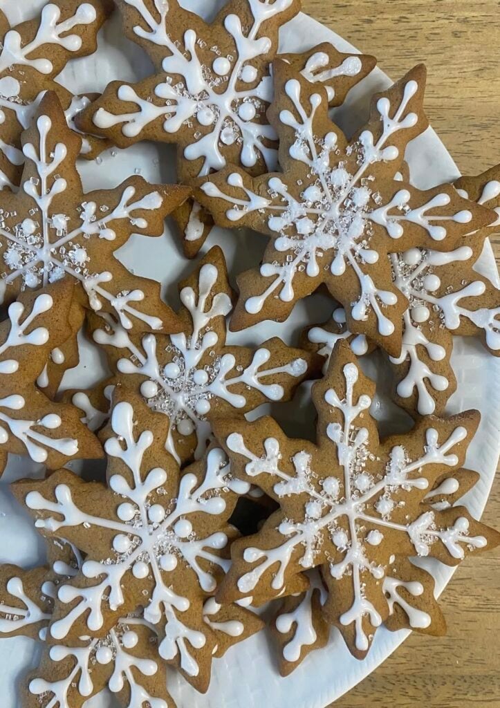Gingerbread cookies shaped like houses and snowflakes on a white background with subtle greenery for Christmas baking.