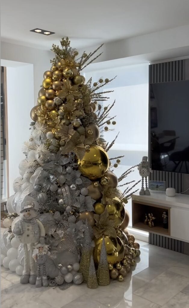 Gold Christmas tree filled with oversized ornaments, ribbon, and luxury holiday decorations.